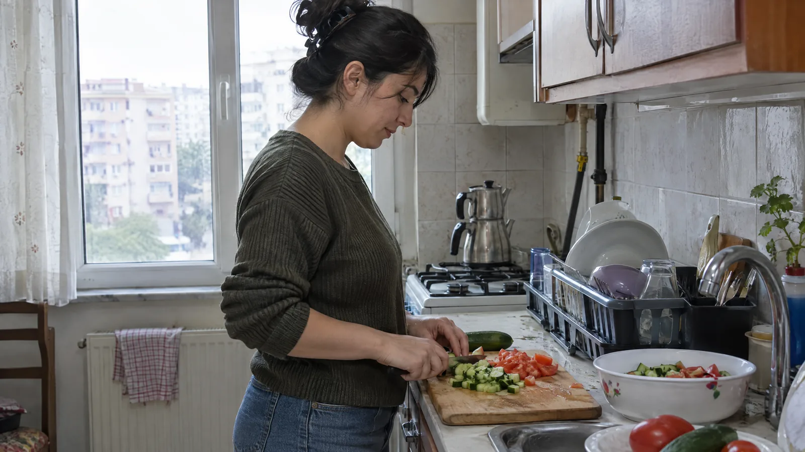 Evinin mutfağında salata için salatalık ve domates doğrayan kadın